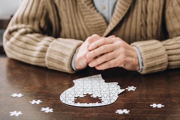 Ein Senior sitzt vor einem Puzzle in Form eines Kopfes, bei dem ein Teil fehlt – Symbol für Demenz und Gedächtnisförderung