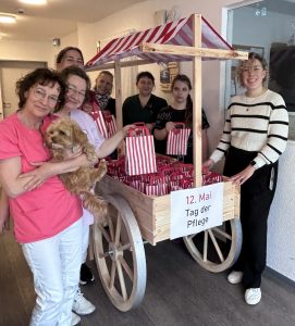 Sieben Frauen und ein kleiner Hund stehen um einen mit Geschenktüten beladenen Holzwagen.