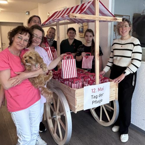 Sieben Frauen und ein kleiner Hund stehen um einen mit Geschenktüten beladenen Holzwagen.