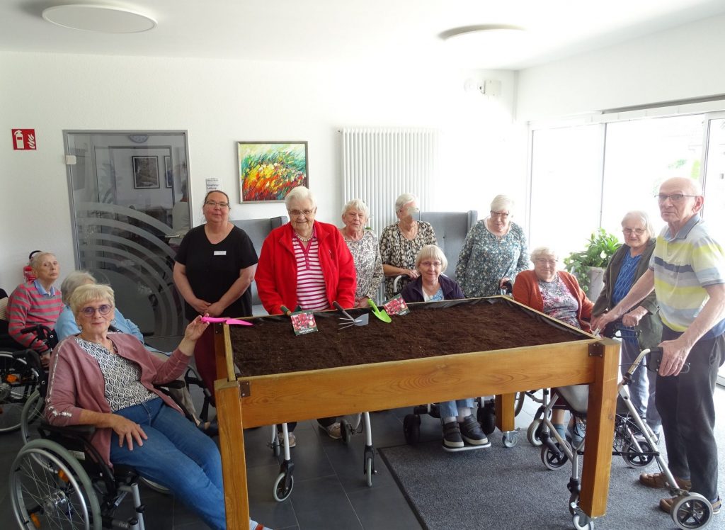 Bewohnerinnen und Bewohner des Haus Phöbe stehen und sitzen um ein Hochbeet