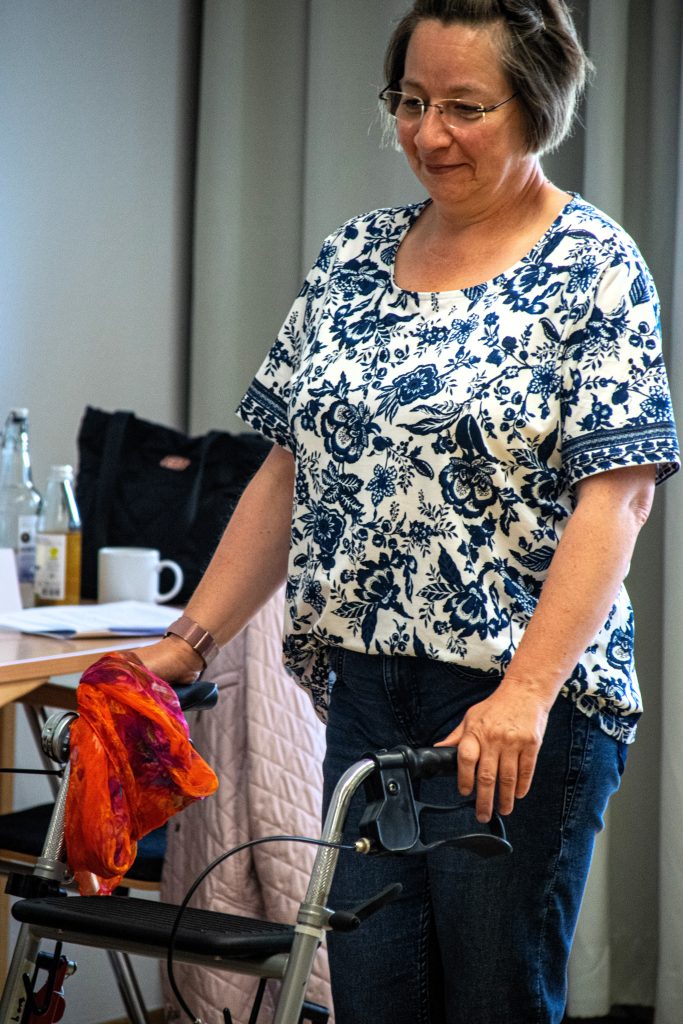Eine Frau steht vor einem Rollator und hat ein rotes Tuch in der Hand.